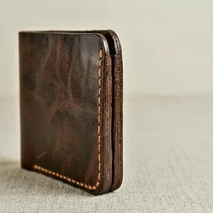 Side view of The Copperhead by Indus Hide, a handmade dark brown full-grain leather bifold wallet featuring contrast amber-gold hand-stitching and six card slots